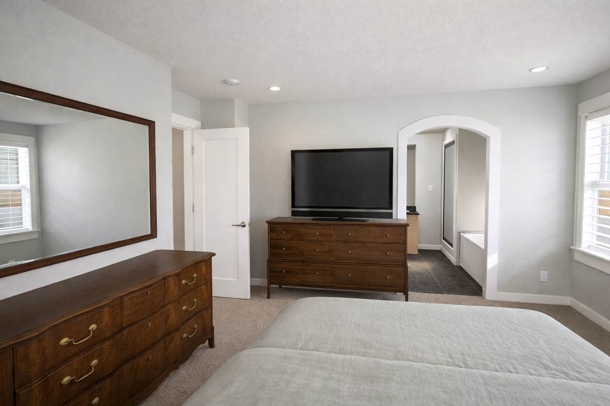 Bedroom with large dresser and mirror, television on dresser, and an arched entryway to an en suite bathroom.