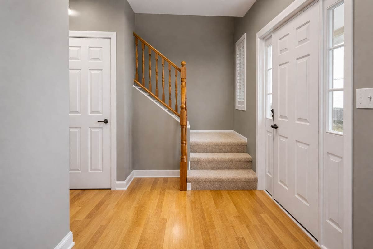 Interior view of entryway with hardwood floors, carpeted stairs, a wood railing, and two white doors.
