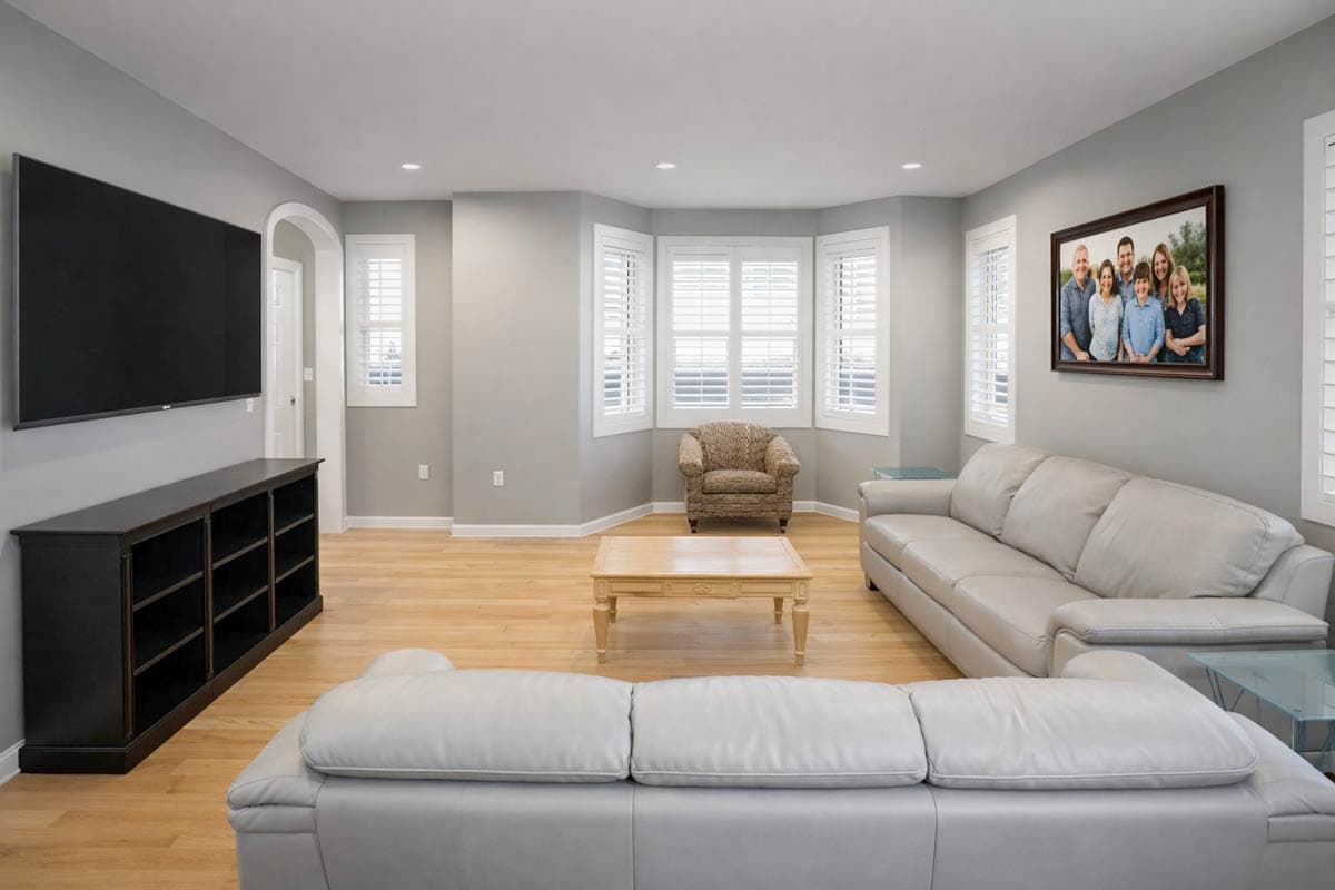 Living room with sectional sofa, accent chair, coffee table, entertainment center, and bay windows with shutters.