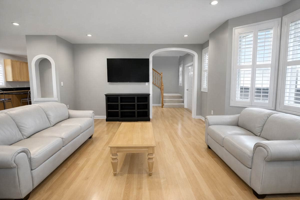 Living room with two sofas, fireplace, black media console, and wood floors. Archway leads to stairs.