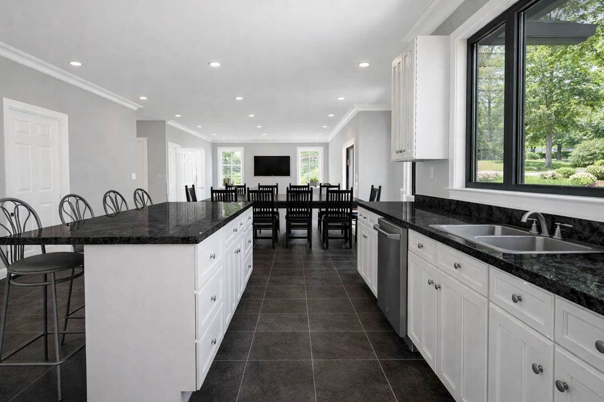 Kitchen with island seating, stainless steel sink, dishwasher, and view into dining area with large table.