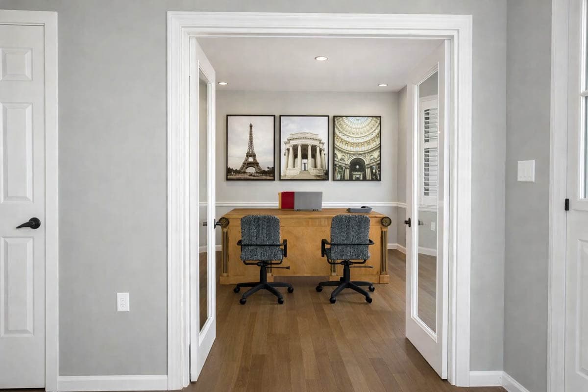 View into an office with a large wooden desk, two chairs, and three framed prints of architectural landmarks.