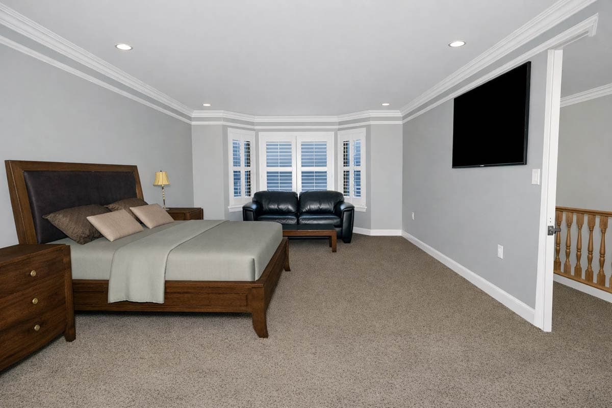 Bedroom with bay window, sofa, bed, dresser, and wall-mounted TV. Staircase visible to the right.