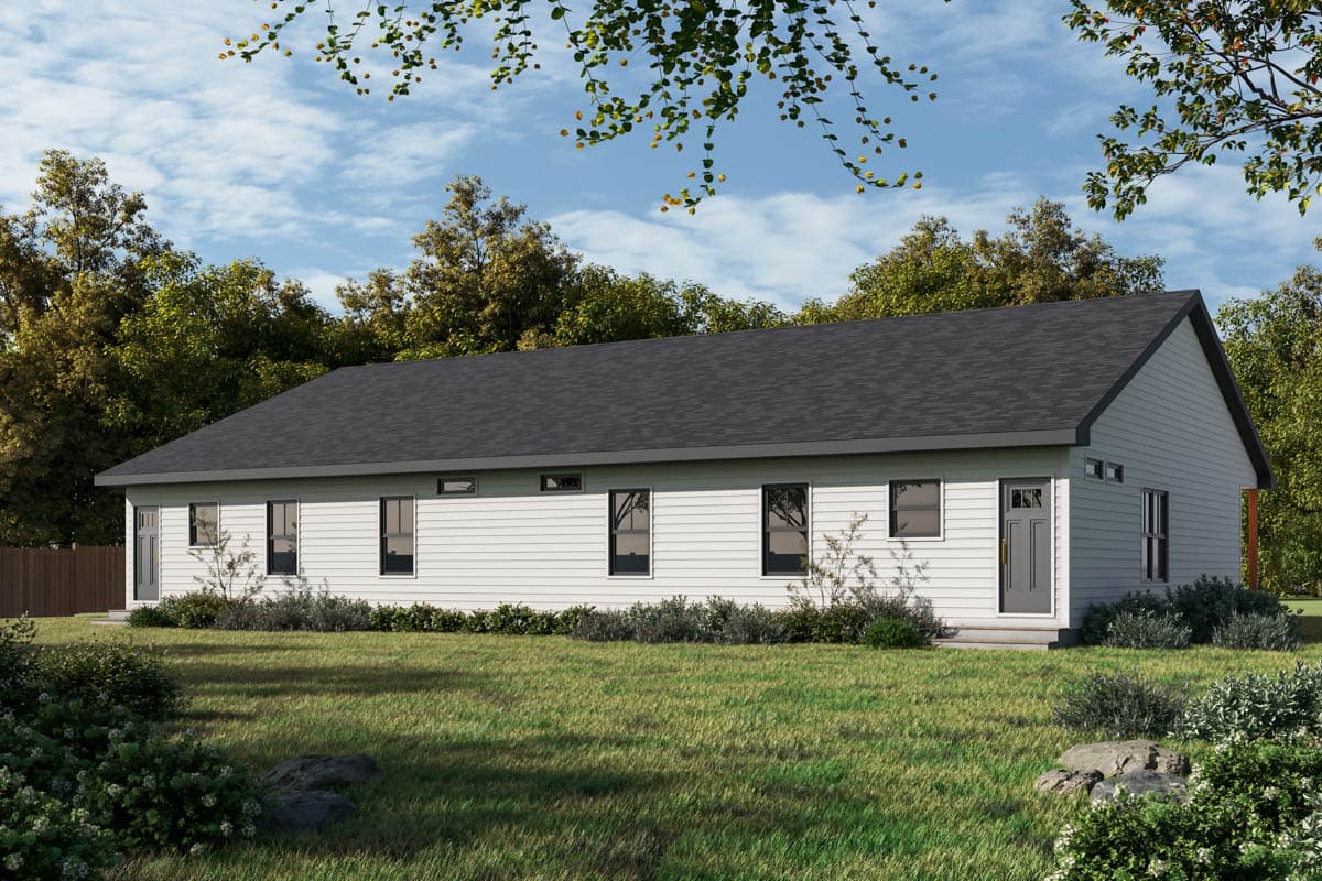 A white, one-story house with a dark gray roof sits on a green lawn surrounded by trees under a partly cloudy sky.