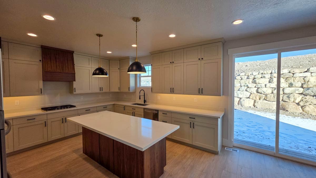 Contemporary kitchen with light wood floors, island, light gray cabinets, dark pendant lights, and a gas range.