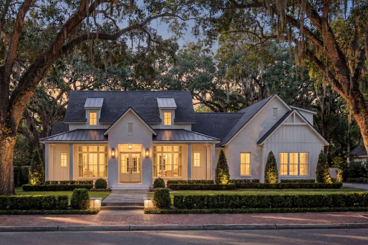 House plan exterior. Modern Farmhouse style, two stories, with a front porch, gables, and dormers. Features include a brick exterior and a dark roof.