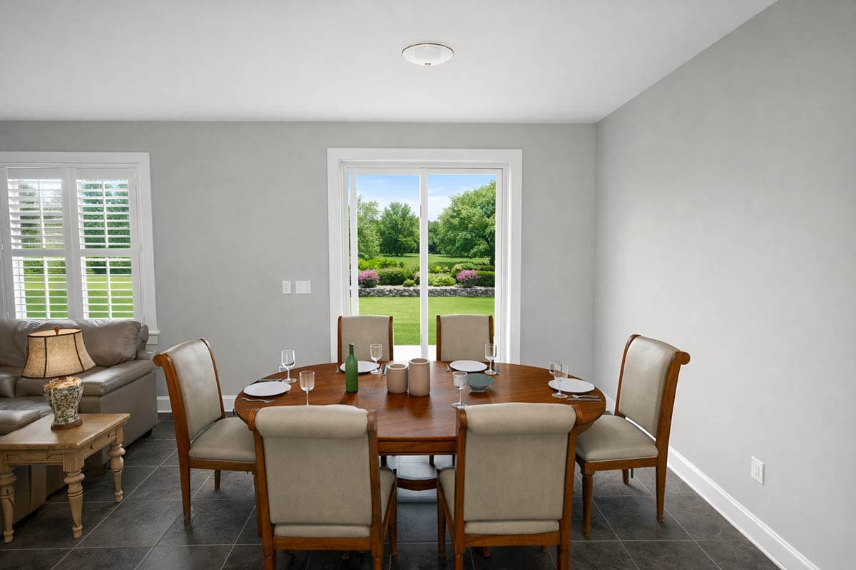 Dining room with oval table, chairs, and large sliding glass door overlooking garden. Adjacent living area with sofa and shuttered window.