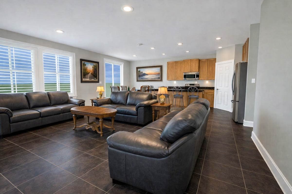 Open-concept living area with dark leather sofas, a coffee table, and a kitchen with wood cabinets and island seating.