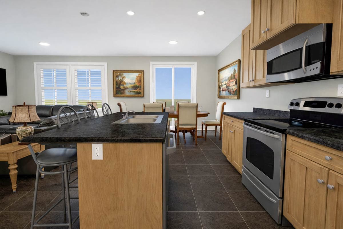 Interior view of a kitchen and dining area with a granite island, wood cabinets, stainless steel appliances, and large windows.