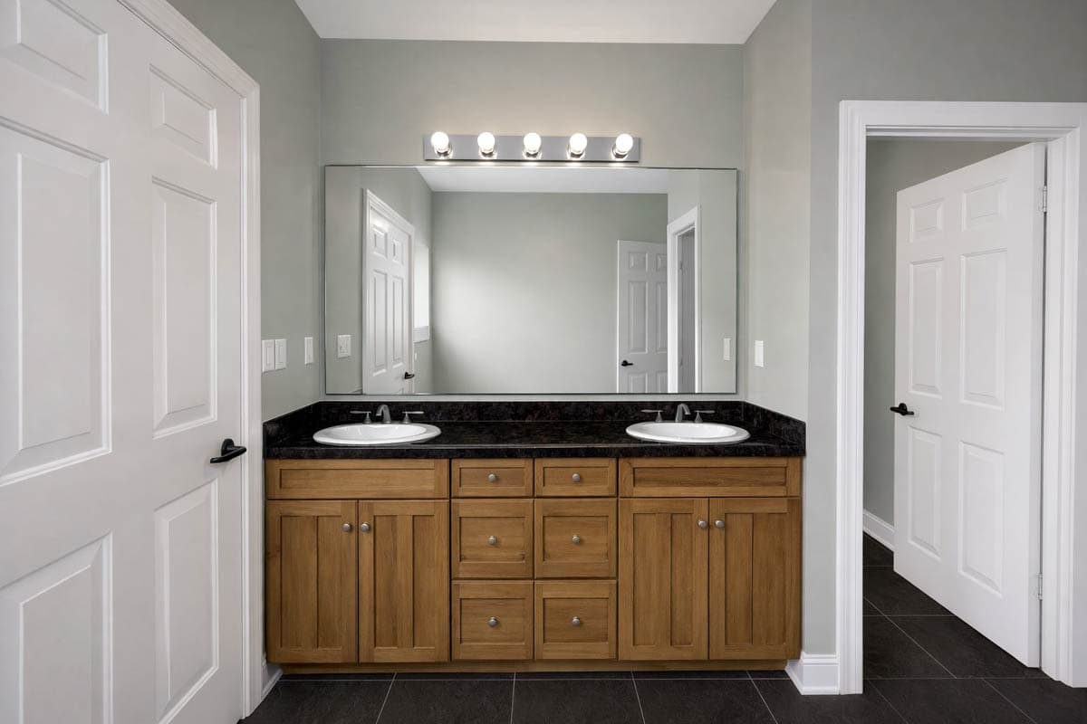 Bathroom featuring a double vanity with wood cabinets, granite countertop, dual sinks, and a large wall mirror.