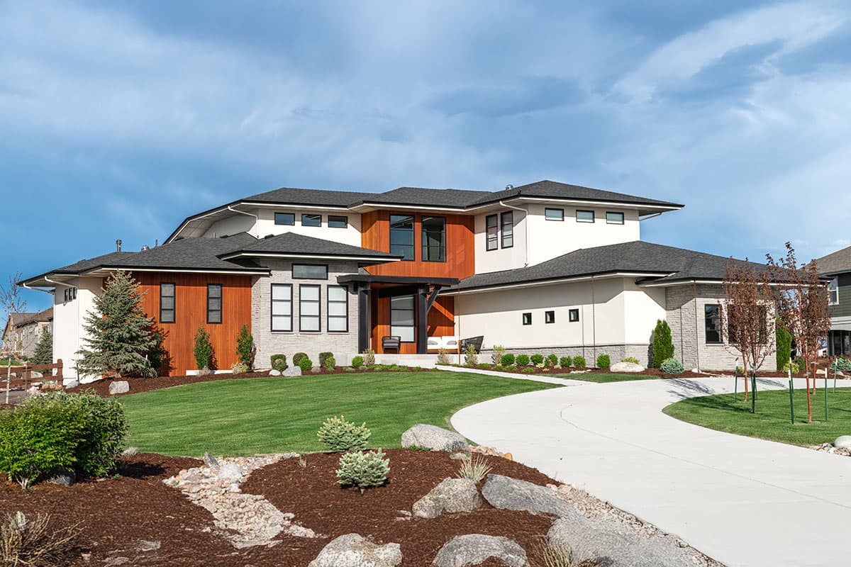 A modern, multi-level home with wood accents and a curved driveway. Lush green lawn and manicured landscaping complement the contemporary design.