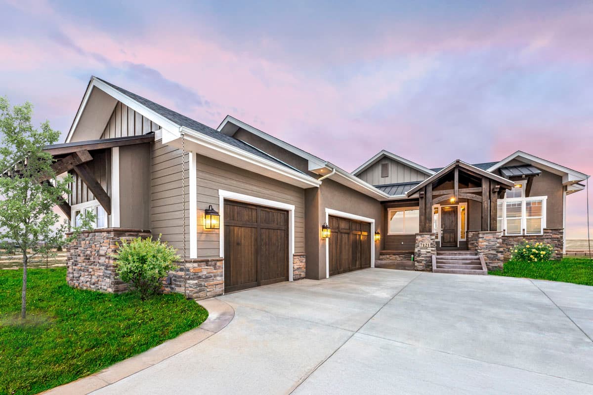 Exterior view of a modern house with two garage doors and a welcoming entrance. Stone accents and wooden beams enhance the design.
