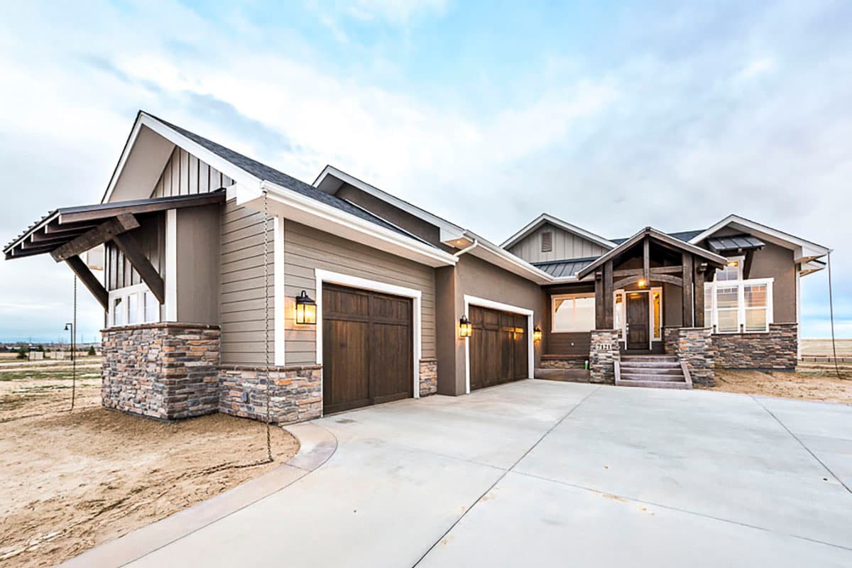 House plan exterior of a two-story Modern Farmhouse with a three-car garage, stone accents, and exposed wooden beams on the porch.