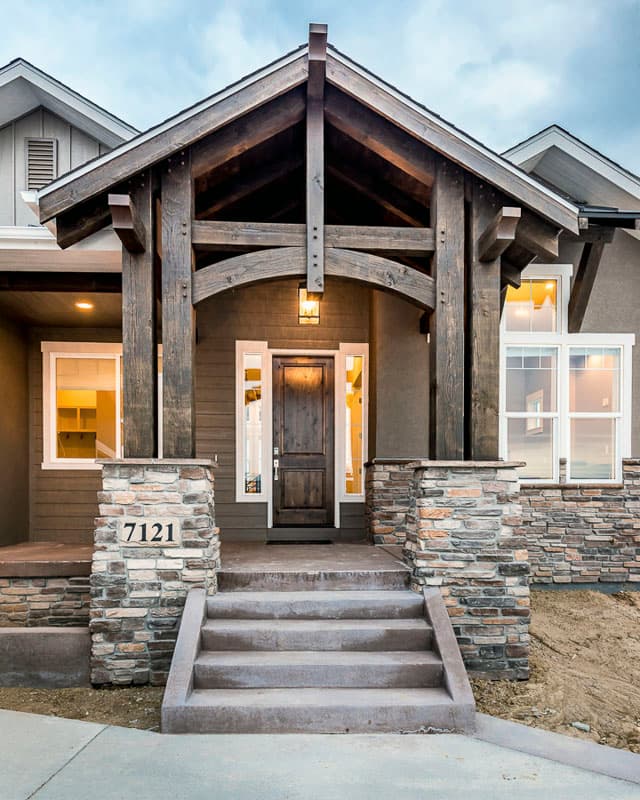 House plan exterior featuring a prominent timber-framed covered entryway with stone-clad pillars and a dark wood door.