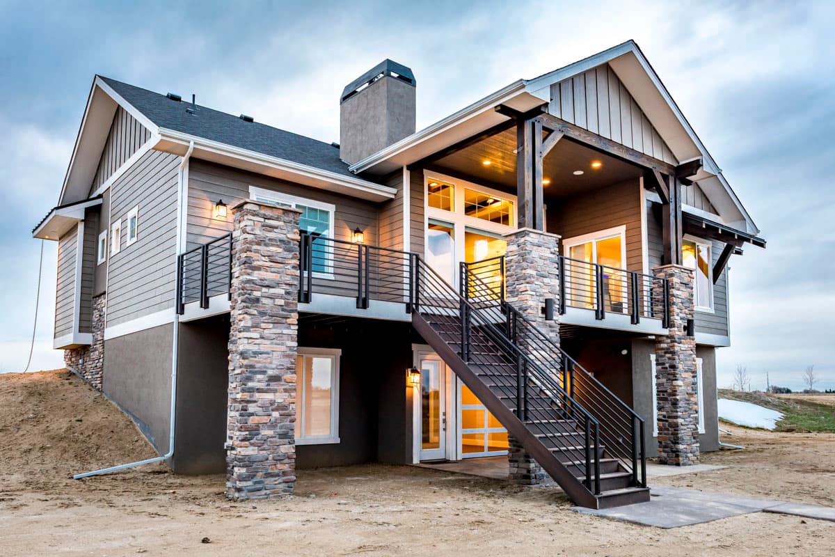 Modern house plan exterior with stone pillars, covered deck, gabled roof, and a prominent central chimney.