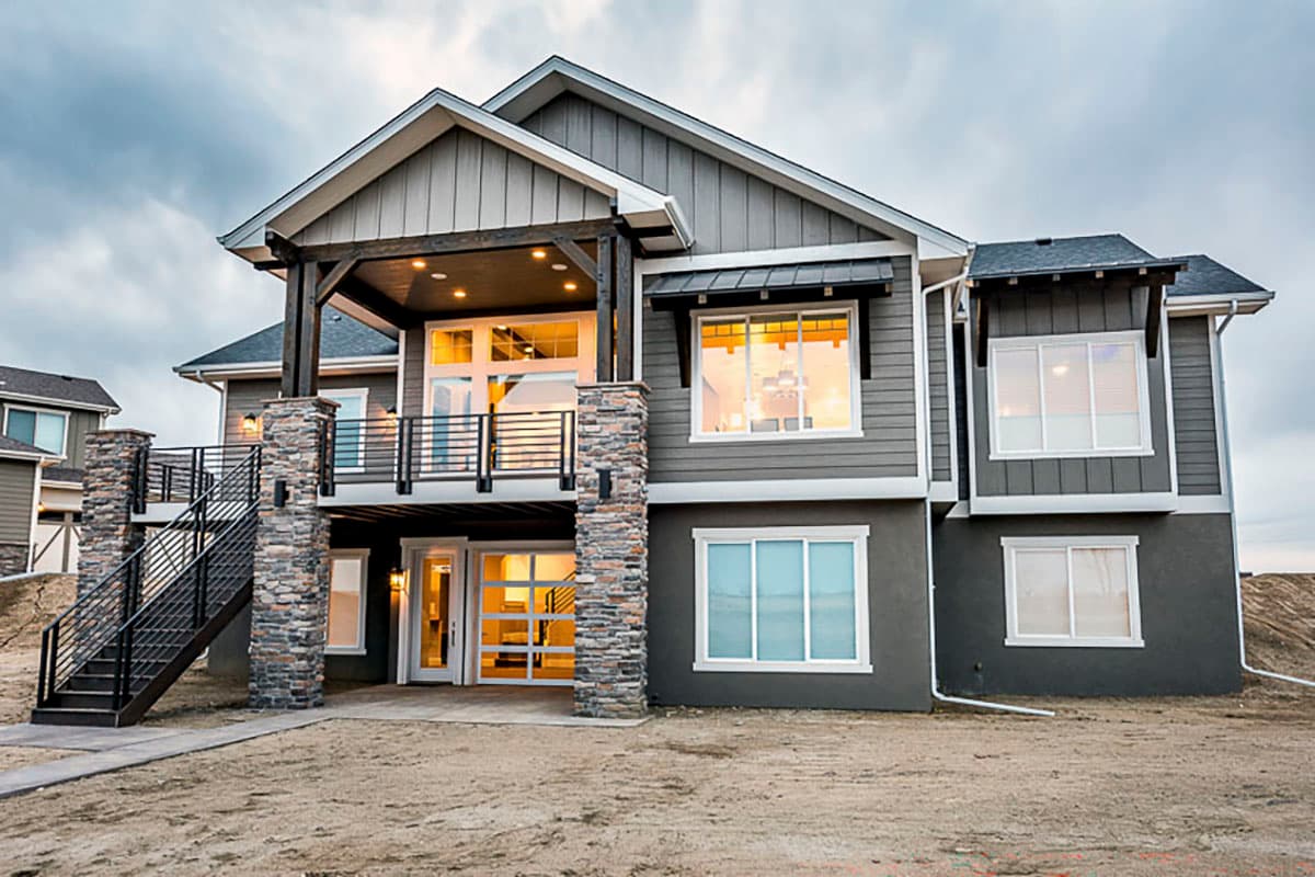 House plan exterior showing a multi-story modern home with stone-clad pillars, a covered balcony, and large windows.