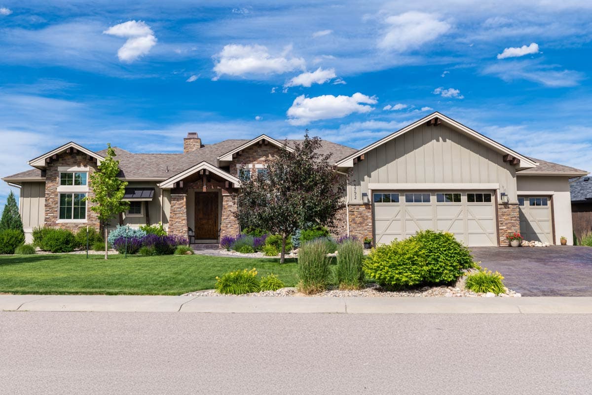 A two-story home with stone accents and a manicured lawn under a bright blue sky. A large garage and front door are visible.