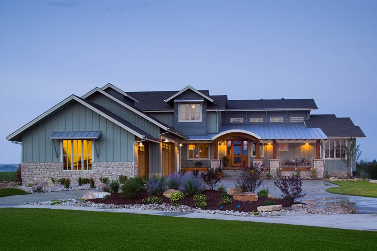 A large, modern home with a blue-gray exterior and a welcoming front entrance. Landscaping with vibrant plants and green lawn. Evening sky backdrop.
