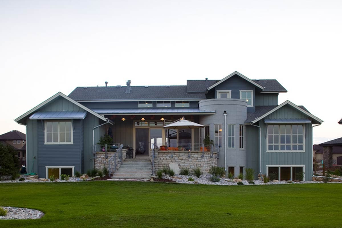 House plan exterior showing a two-story home with gables, a circular tower, and a raised stone patio with stairs.
