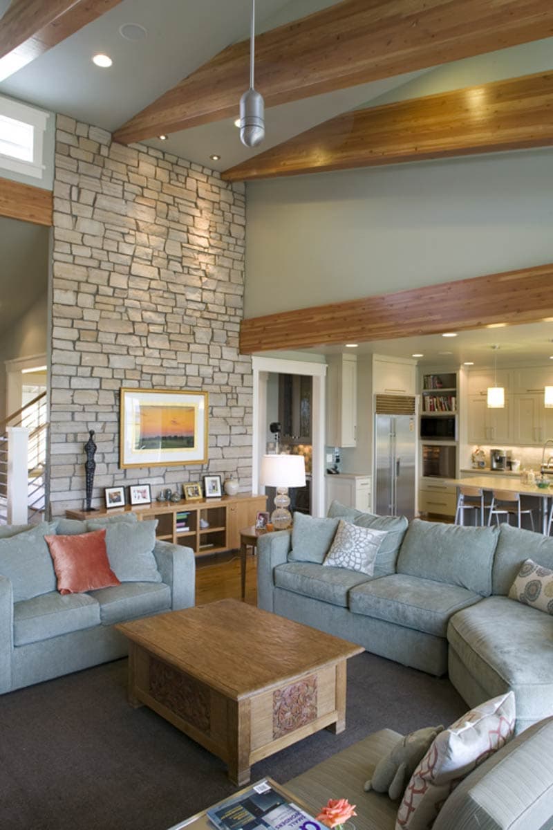 Great room with vaulted ceiling, exposed beams, stone accent wall, sectional sofa, and open kitchen with island.