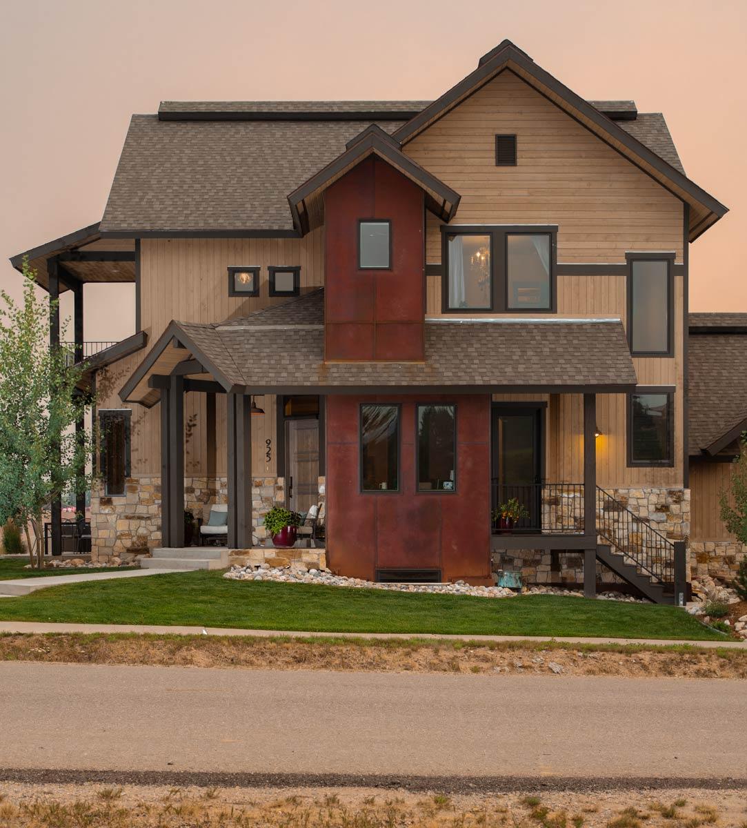 House plan exterior with a two-story design, wood siding, stone accents, gable roofs, and a covered front porch.