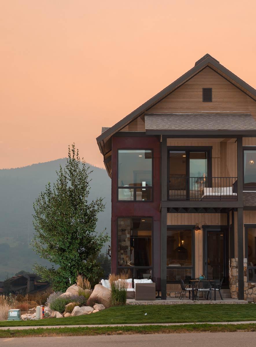 House plan exterior with modern rustic design, wood siding, stone accents, large windows, and covered balcony.