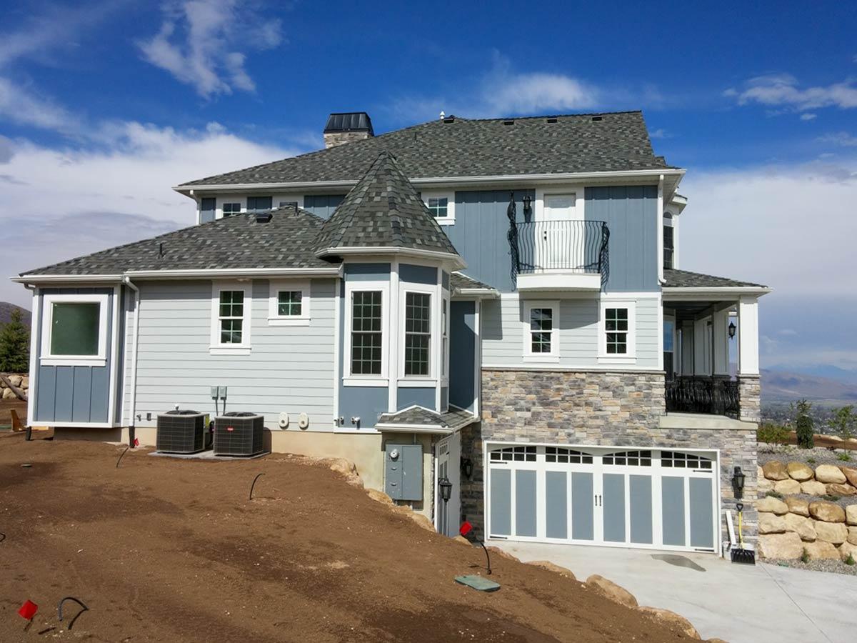 House plan exterior: three-story home with stone and lap siding, turreted bay window, balcony, and multi-car garage.