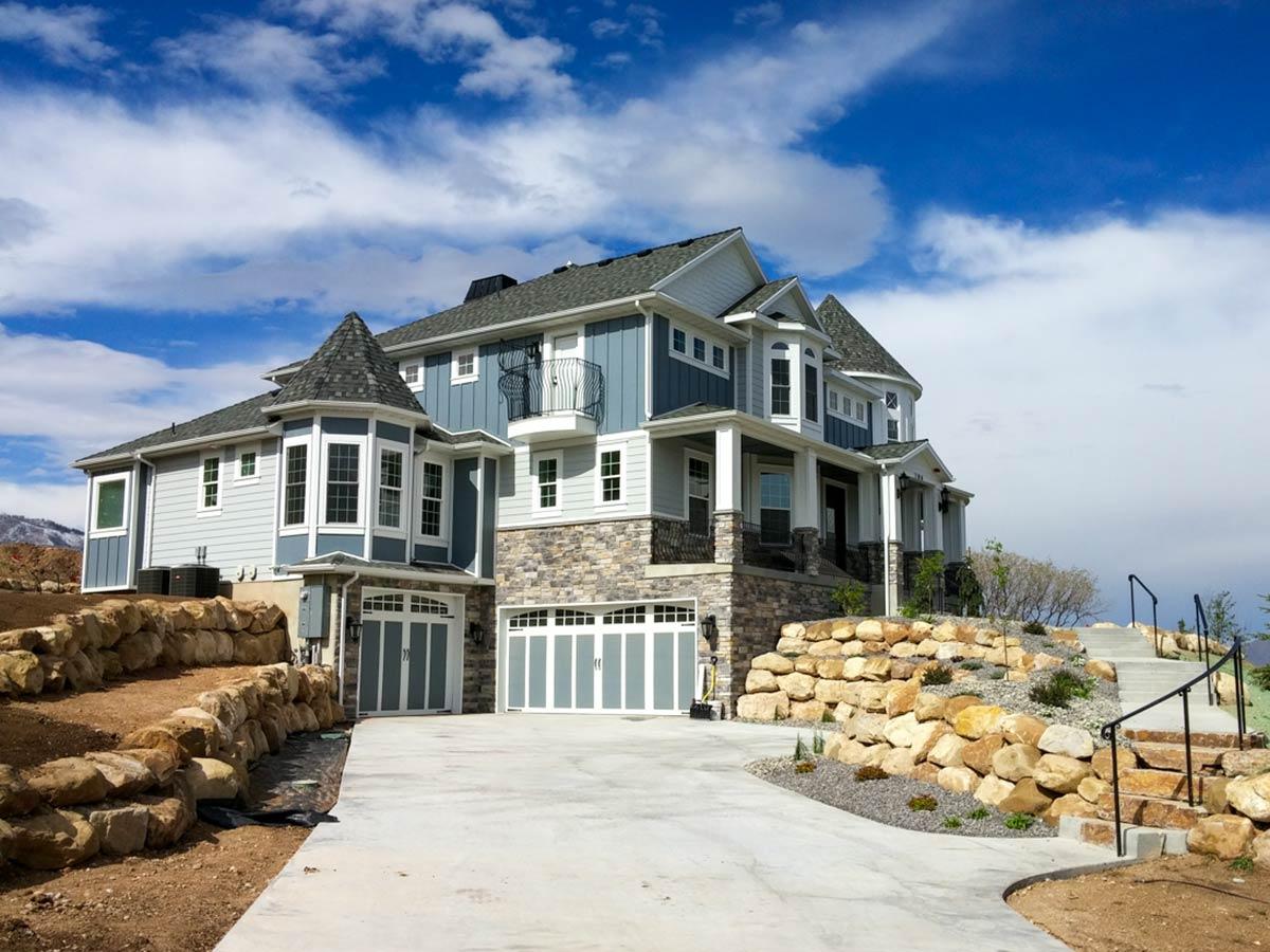 House plan exterior: Modern home with stone facade, multiple gables, a turret, bay windows, and a three-car garage.
