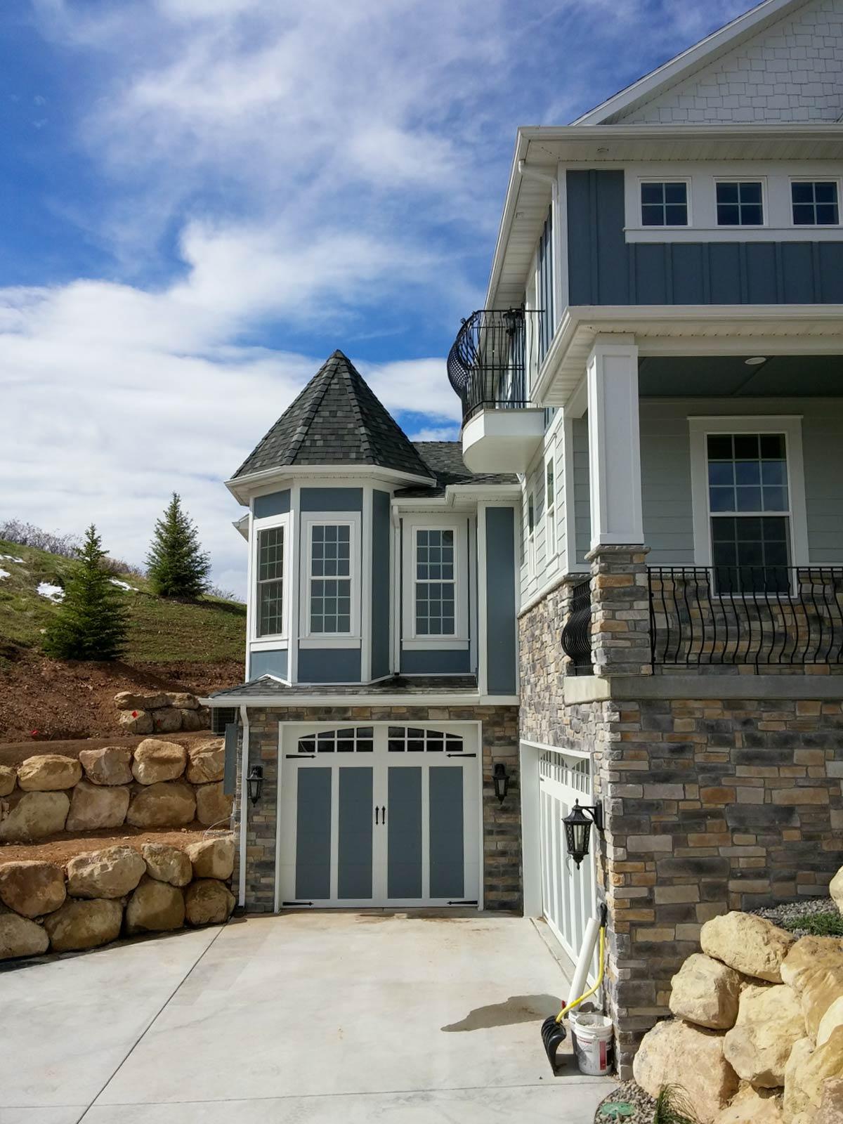 House plan exterior featuring a turretted bay window, multi-story siding, stone accent, and a two-car garage.