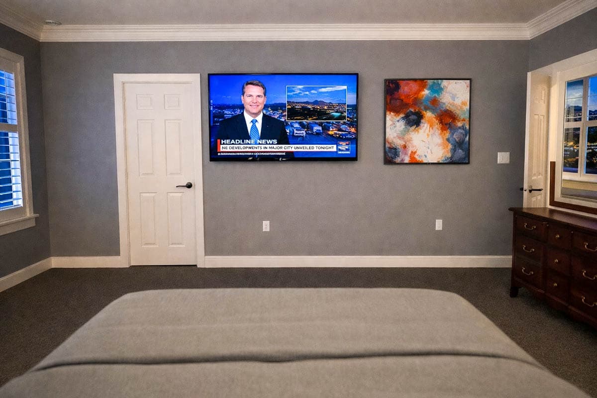 Bedroom with gray walls, white paneled door, mounted television, abstract art, and wooden dresser.