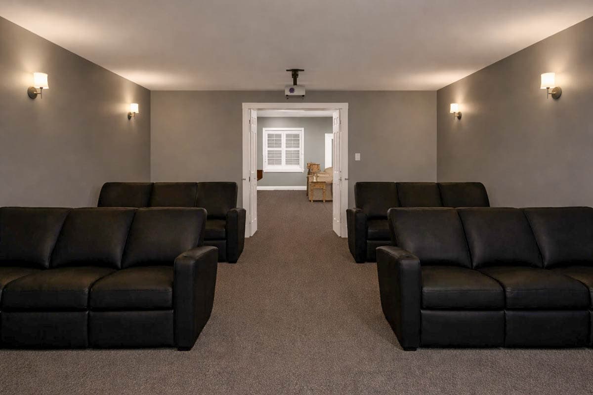 Home theater room with multiple rows of black leather sofas and a projector mounted on the ceiling.