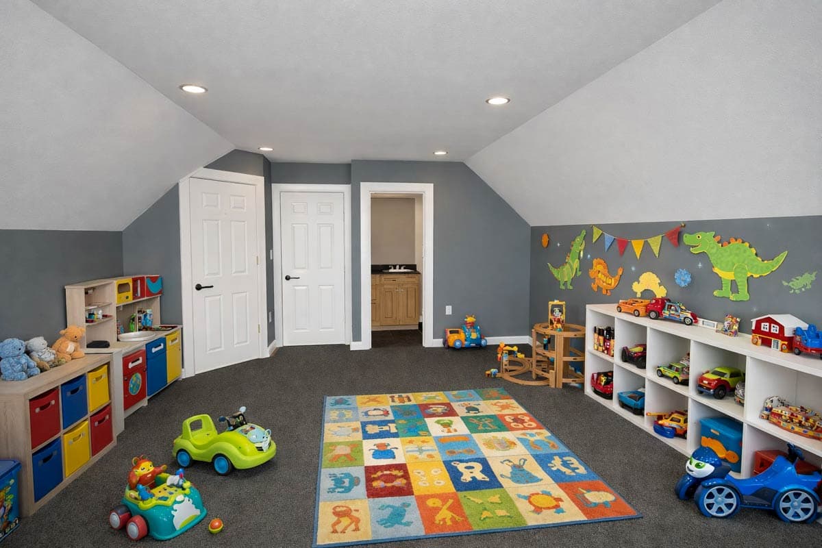 Children's playroom with toy storage shelves, a colorful rug, and dinosaur wall decals. Two doors and a partial view of a bathroom are visible.