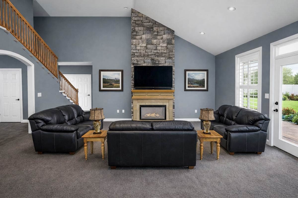 Interior view of a great room with a stone fireplace, vaulted ceiling, wooden staircase, and two doorways.
