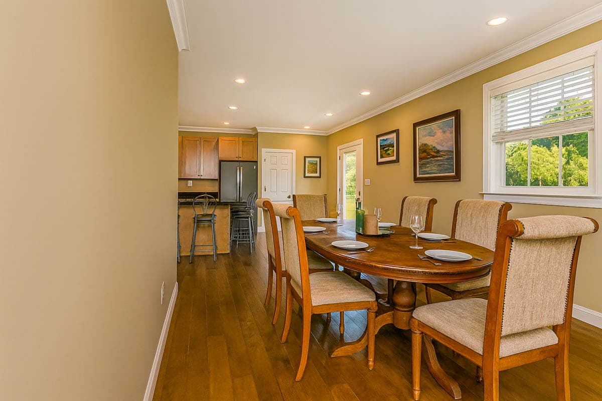 Dining area with oval wood table and chairs. Kitchen area with island, stools, and refrigerator visible.