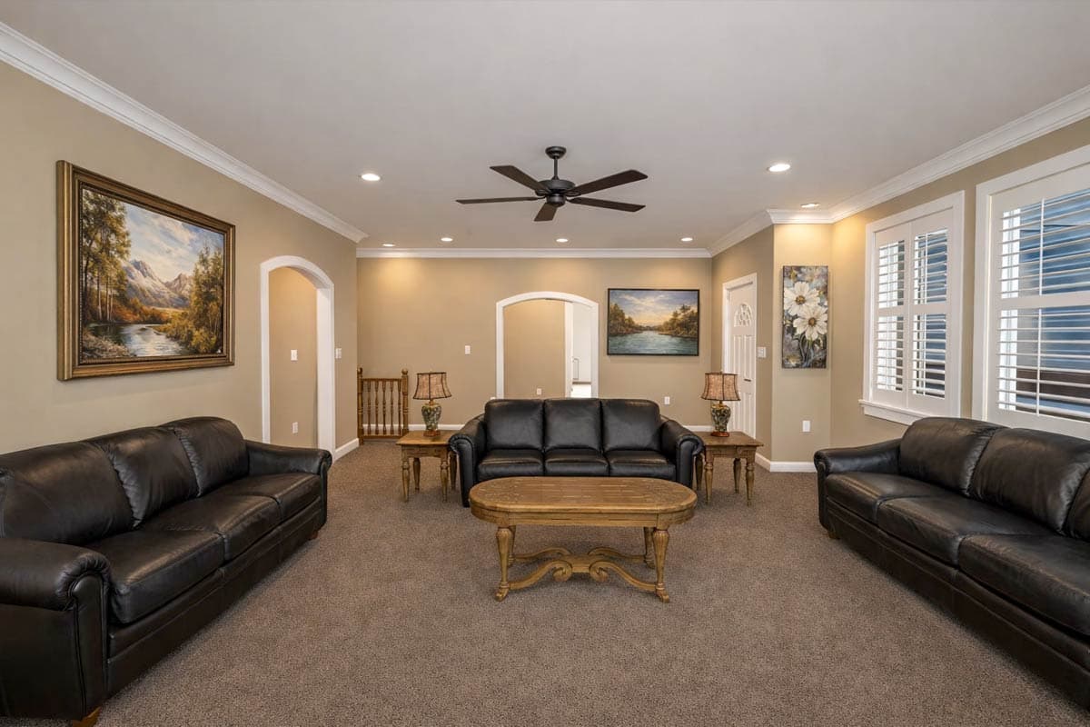 Interior view of a living room with black leather sofas, a wooden coffee table, a ceiling fan, and arched doorways.
