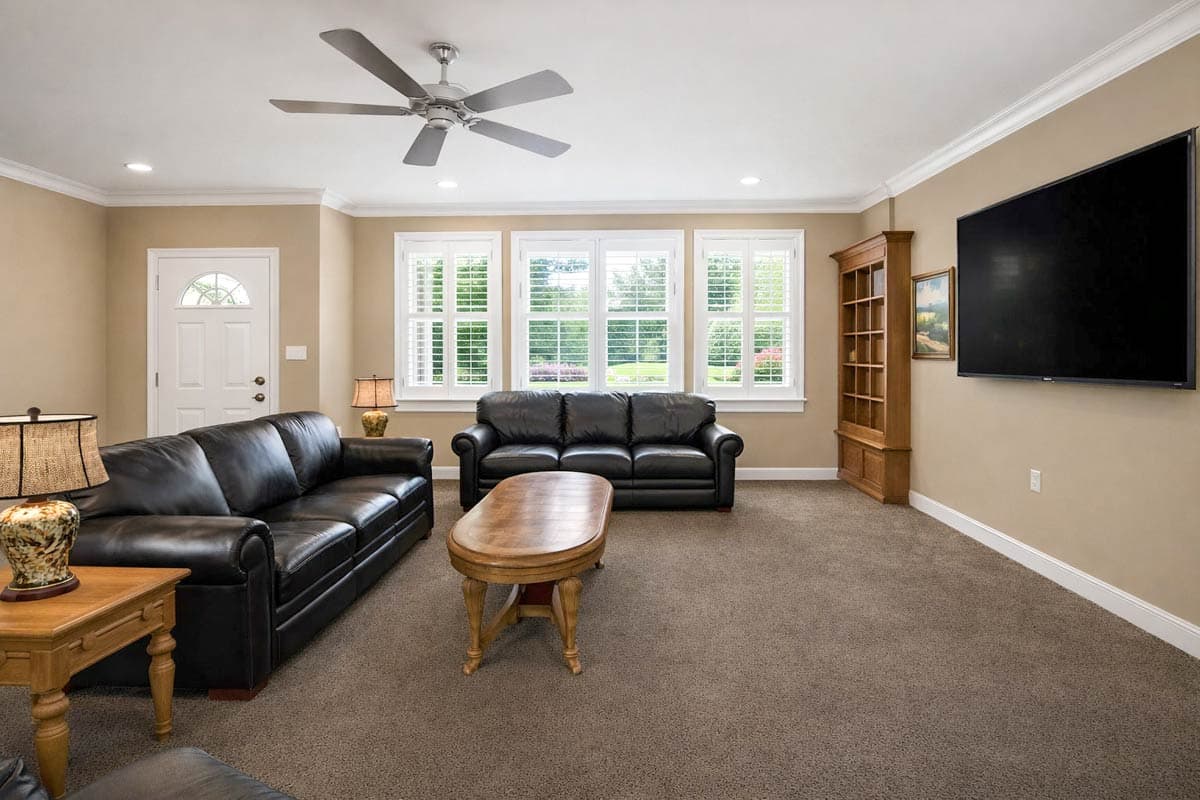 Living room with black leather sofas, oval coffee table, built-in bookshelf, and wall-mounted television.