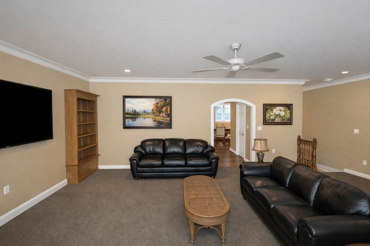 Living room with two black leather sofas, wooden bookcase, television, and an arched doorway to dining area.