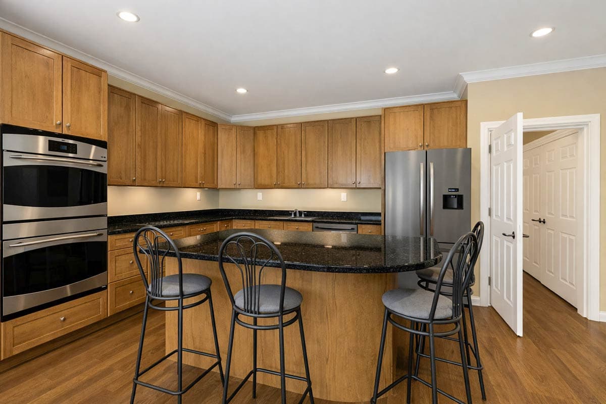 Kitchen with wood cabinetry, granite countertops, island with seating, stainless steel double ovens, and stainless steel refrigerator.