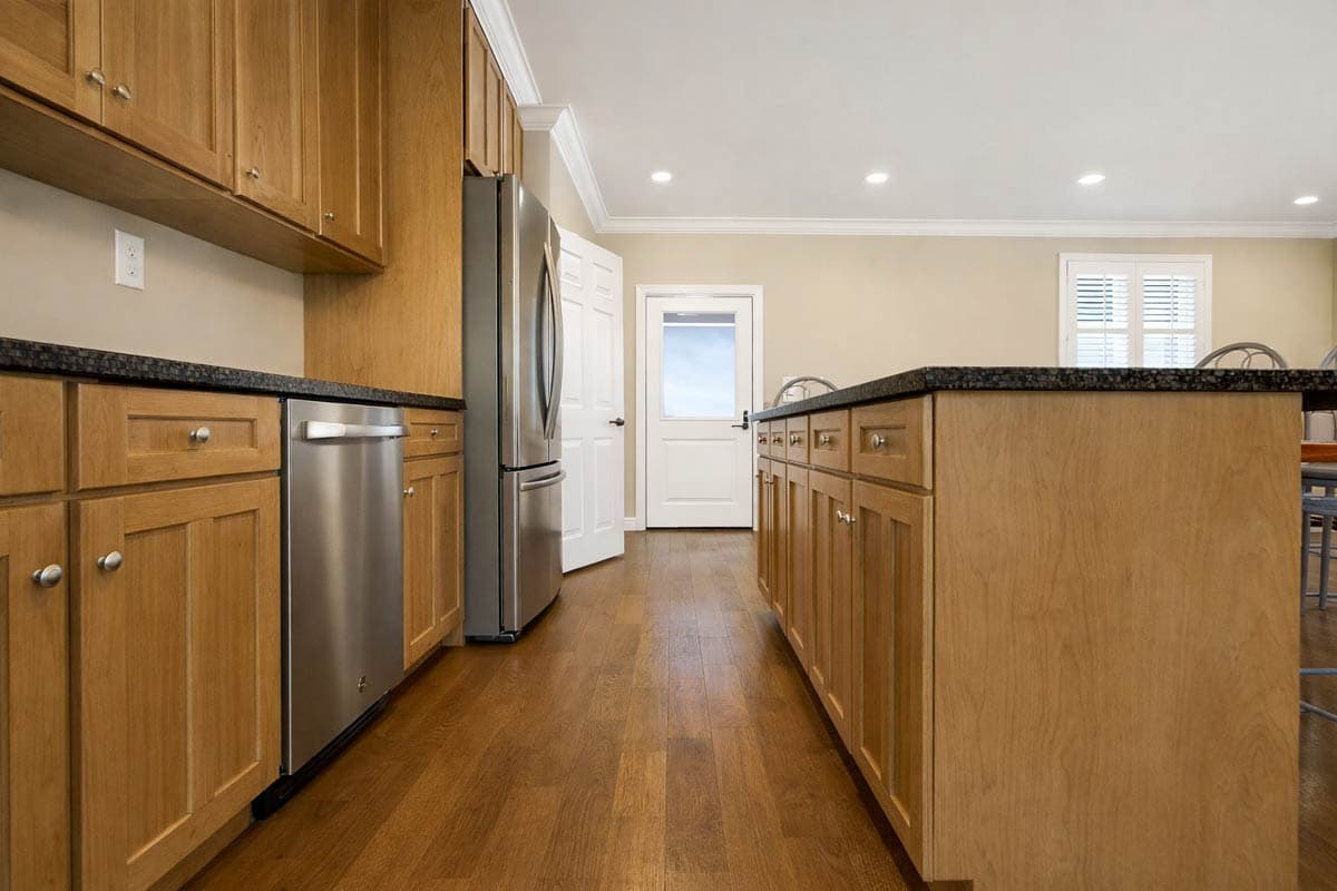 Kitchen with light wood cabinets, stainless steel appliances including dishwasher and refrigerator, and a center island with granite countertop.