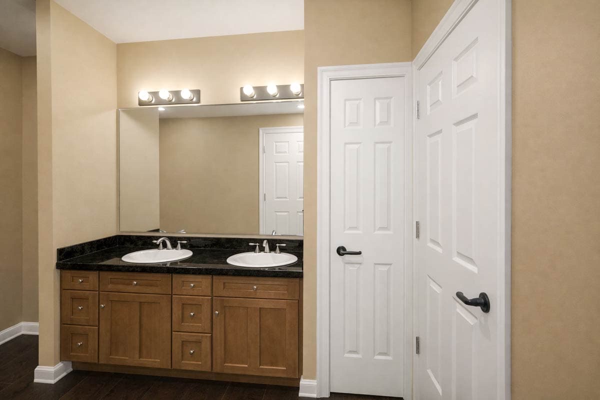Bathroom vanity with double sinks and granite countertop, adjacent to two white paneled doors.