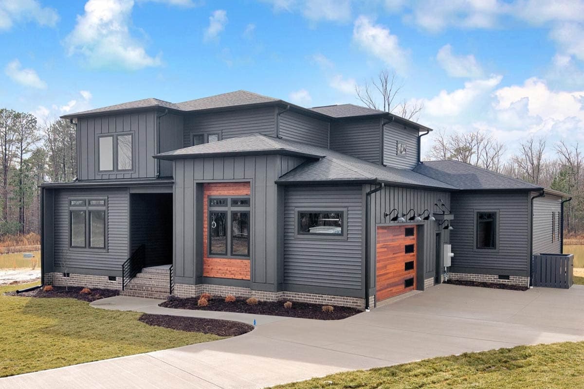 Modern two-story house plan exterior with dark gray siding, wood accents, prominent gables, and a modern garage door.