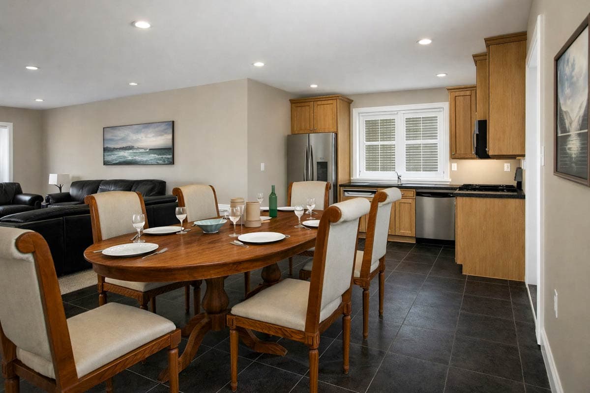 Dining area with oval wood table and chairs, adjacent to a kitchen with wood cabinets, stainless steel appliances and window.