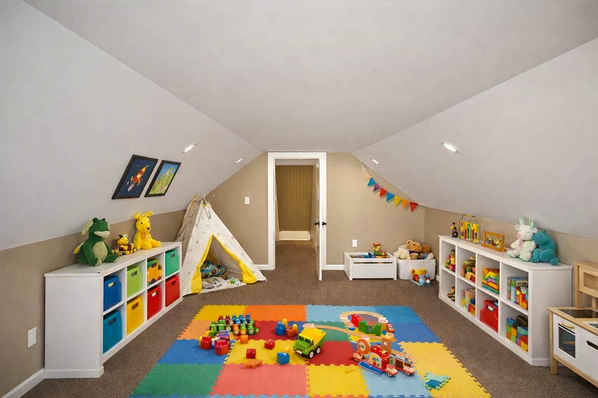 Interior view of a child's playroom with slanted ceilings, toy storage shelves, a teepee, and a colorful foam floor mat.