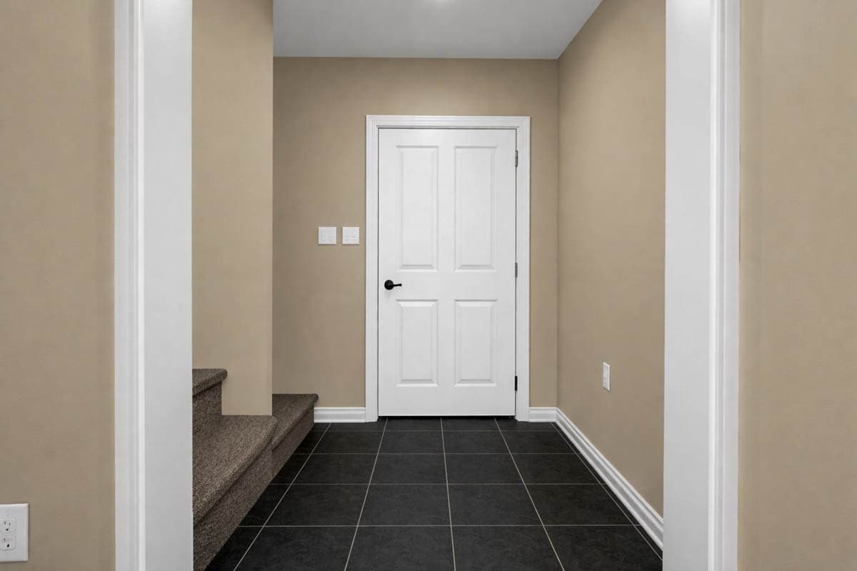 Interior hallway with neutral walls, carpeted stairs, white door, and black tile floor.
