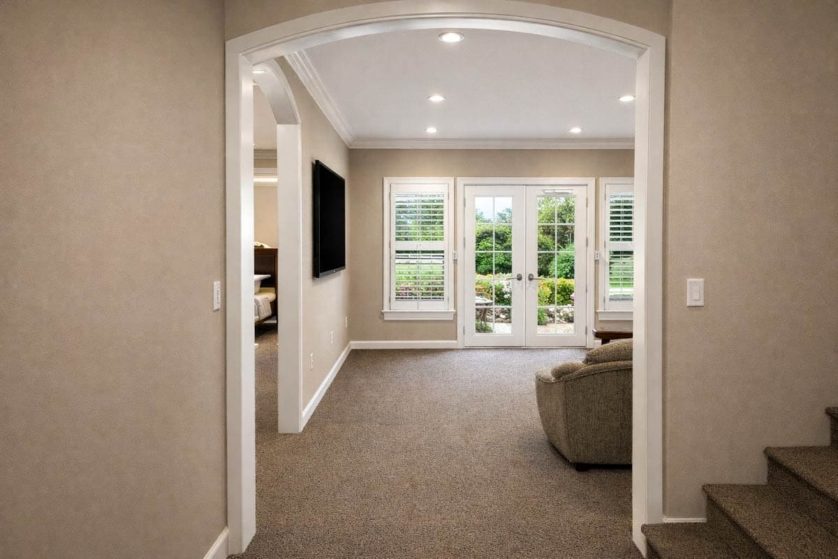 Living room with plush carpet, large windows, double doors to backyard, and an archway leading to another room.