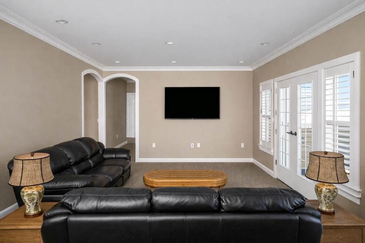 Living room interior with black leather sofas, wood coffee table, wall-mounted TV, and French doors with shutters.