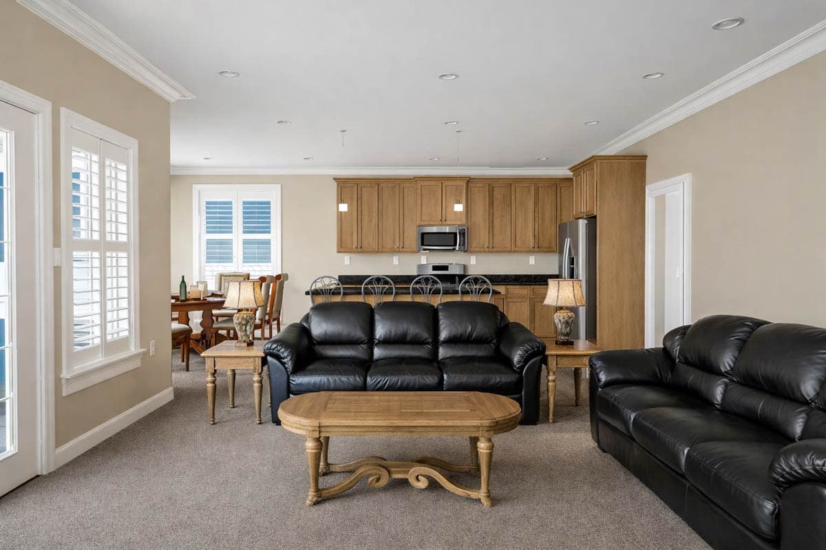 Living area with two black leather sofas and a dining area adjacent to a kitchen with wood cabinets.
