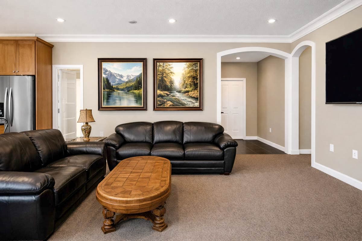 Interior view: Living area with leather sofas, wooden coffee table, two landscape paintings, and an arched doorway leading to a hall.