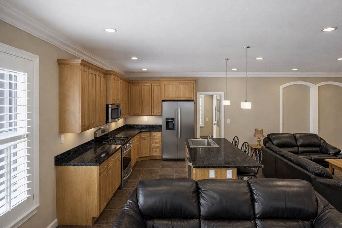 Open concept kitchen with wood cabinets, granite island, and stainless steel appliances, flows into a living area.