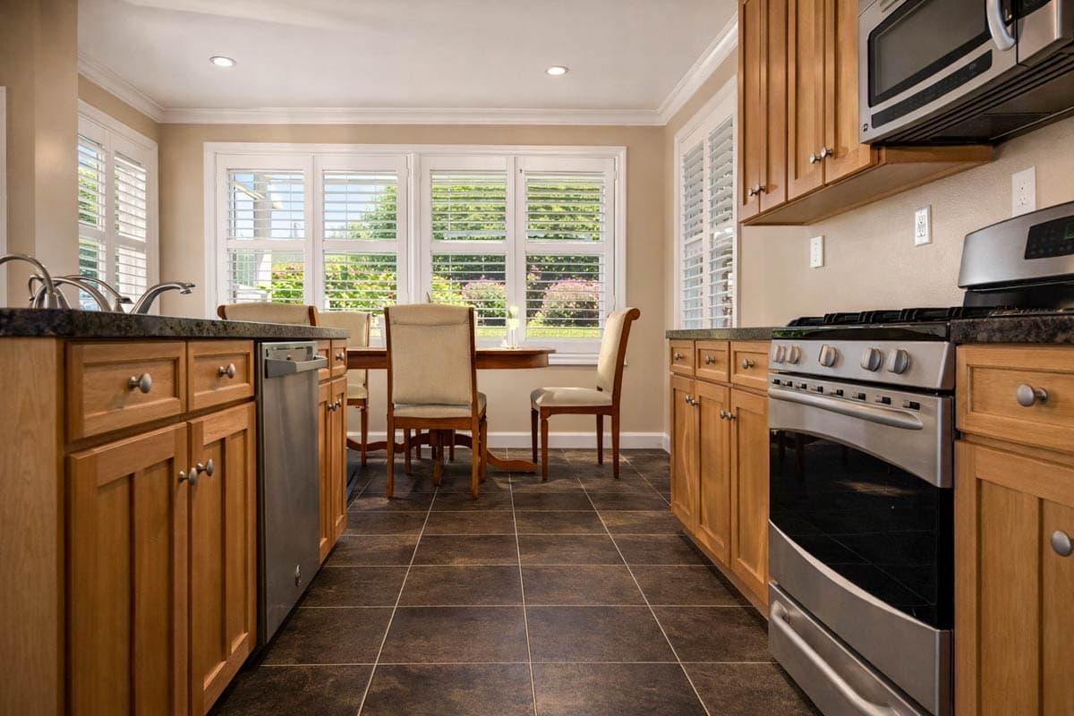 Kitchen with wood cabinets, granite countertops, stainless steel appliances, and a dining area with plantation shutters.